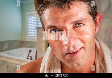 stile di vita home ritratto di giovane felice e attraente uomo con occhi blu che asciugano con asciugamano dopo doccia in bagno sorridente allegro in hygi quotidiano Foto Stock