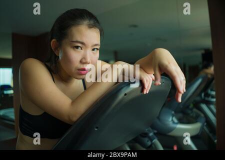 Giovane attraente e in forma Asian Chinese donna esausta durante l'allenamento in corsa presso la palestra dell'hotel o club fitness che fa jogging nella tapis roulant allenandosi duramente con tir Foto Stock