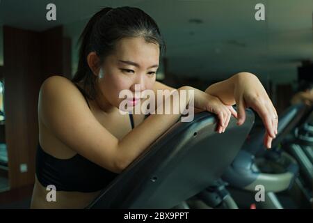 Giovane attraente e in forma Asian Korean donna esausta durante l'allenamento in corsa presso la palestra dell'hotel o club fitness che fa jogging nella tapis roulant allenandosi duramente con gli pneumatici Foto Stock