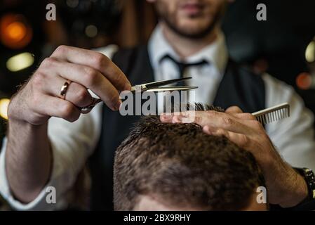 Le mani del Barbiere tagliano i capelli con forbici, primo piano, abiti classici, cravatta e camicia Foto Stock