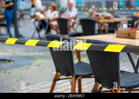 Terrazze in città di nuovo aperto. Il nastro di sicurezza sulla terrazza garantisce la possibilità di mantenere una distanza sociale sicura tra i tavoli e le sedie durante il coronavirus Foto Stock