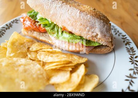 Panino di bacon e pomodoro fritto e baguette alla lattuga, talvolta chiamato BLT su un piatto bianco con una finitura dorata con patatine fritte. Su un tavolo di legno Foto Stock