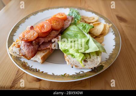 Pancetta fatta in casa e pomodoro fritto e baguette lattuga, a volte chiamato BLT prima di chiudere su un piatto bianco con una finitura dorata con croccante Foto Stock