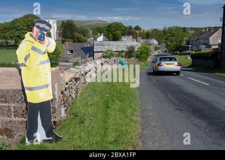 Taglio di cartone di un poliziotto che tiene una pistola ad alta velocità per aiutare il traffico lento sull'avvicinamento ad un villaggio. Cumbria, Regno Unito. Foto Stock