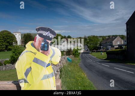 Taglio di cartone di un poliziotto che tiene una pistola ad alta velocità per aiutare il traffico lento sull'avvicinamento ad un villaggio. Cumbria, Regno Unito. Foto Stock