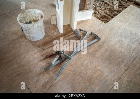 in un cantiere due morsetti in acciaio, un martello grande e un cucchiaio sono affiancati Foto Stock