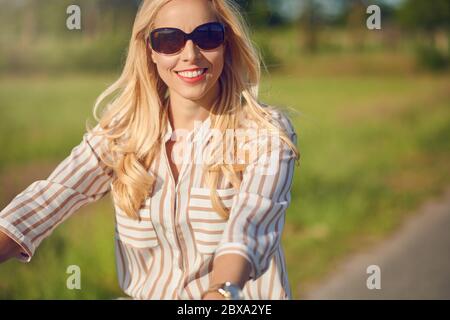 Ritratto di una bella donna sorridente felice mentre indossa una camicia a righe e cavalcare una bicicletta in campagna in una giornata di sole Foto Stock
