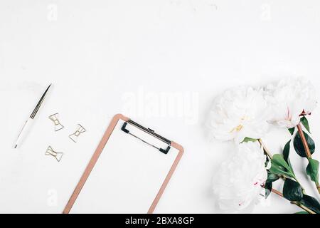 Scrivania da tavolo per ufficio. Luogo di lavoro con tazza di caffè, fiori peonie, penna, appunti. Disposizione piatta, vista dall'alto, mockup, spazio per la copia. Note o concetto di pianificazione Foto Stock