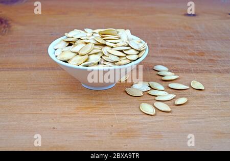 Piatto di semi di zucca organici e semi di zucca versato su sfondo di legno Foto Stock