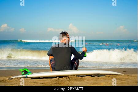 ritratto di stile di vita di attraente e felice uomo surfista 3os a 40s in neoprene surf costume in posa con surf tavolo seduto sulla spiaggia di sabbia godendo ho Foto Stock