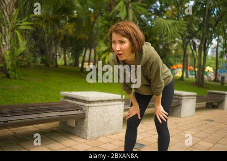 ritratto all'aperto di giovane attraente donna jogger stanco e senza fiato in respirazione esaurita dopo l'allenamento in esecuzione nel bellissimo parco cittadino in forma fisica Foto Stock