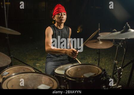 Asian American teenager misto suonare batteria in giardino di casa. Fresco e bel ragazzo giovane che pratica su drum kit provando appassionato in roccia di badass b Foto Stock