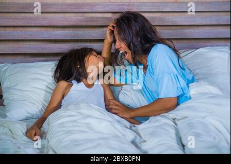 Stile di vita ritratto camera da letto di felice donna asiatica a casa giocando con piccola figlia in letto coccolando e ridendo allegro in madre e bambino amore an Foto Stock