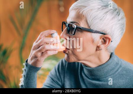 Donna anziana che usa l'inalatore per asma con tubo di prolunga Foto Stock