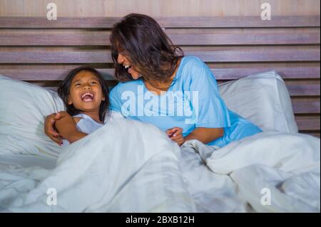 Stile di vita ritratto camera da letto di felice donna asiatica a casa giocando con piccola figlia in letto coccolando e ridendo allegro in madre e bambino amore an Foto Stock