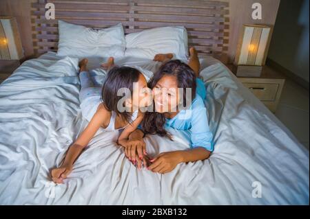 Stile di vita ritratto camera da letto di felice donna asiatica a casa in posa con la sua bella figlia di 8 anni in letto sorridente allegro allegro in madre e. Foto Stock