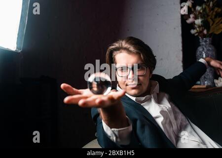 Giovane uomo che tiene in mano una palla trasparente trasparente di cristallo Foto Stock