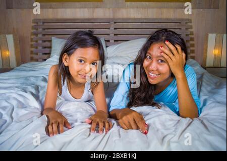 Stile di vita ritratto camera da letto di felice donna asiatica a casa in posa con la sua bella figlia di 8 anni in letto sorridente allegro allegro in madre e. Foto Stock