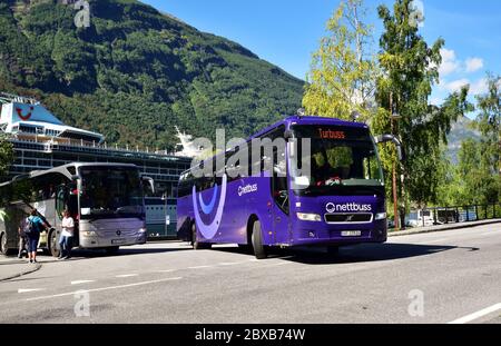 Nettbuss Volvo B12B UF 37926 esce dal punto di partenza del pullman a Geiranger, Norvegia, mentre i turisti salono a bordo di un pullman Mercedes-Benz Tourismo. Foto Stock