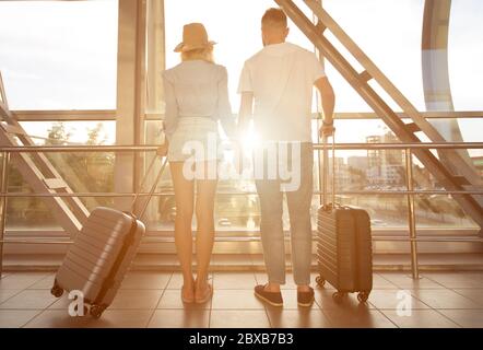 Vista posteriore della coppia in piedi in aeroporto con bagagli Foto Stock