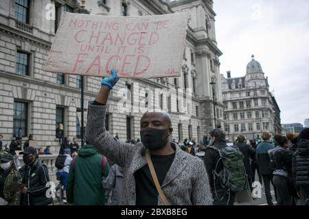 Un protetore passa davanti agli edifici istituzionali nel centro di Londra, con un cartello contro il razzismo sistemico nel Regno Unito. Foto Stock