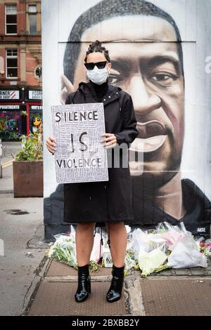 Un protettrice che tiene un cartello si trova di fronte ad un murale dipinto dall'artista di strada AKSE P19 durante la manifestazione. Diverse proteste sono state scatenate dalla recente uccisione di George Floyd, un uomo nero morto in custodia di polizia a Minneapolis, U.S.A. Foto Stock