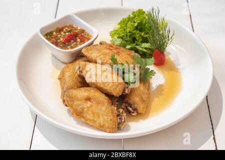 Ali di pollo fritte con salsa di pesce su piatto bianco e tavolo di legno bianco Foto Stock