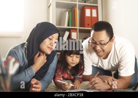 Genitori musulmani asiatici che disegnano con la loro figlia, madre e padre insegnano la bambina, imparando sul pavimento, concetto felice di famiglia Foto Stock