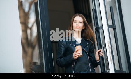 Giovane donna che esce dall'edificio urbano attraverso una grande porta di vetro Foto Stock