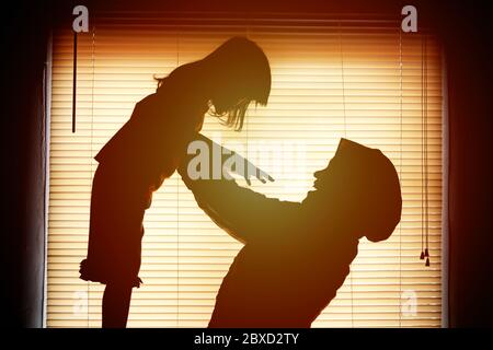 La madre felice e la sua ragazza del bambino che giocano insieme, silhouette del tramonto, la mom tiene e solleva il suo capretto in su nell'aria Foto Stock