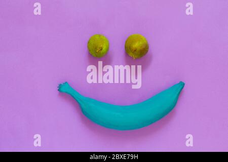 banana rosa con due pere a forma di volto sorridente su sfondo viola Foto Stock