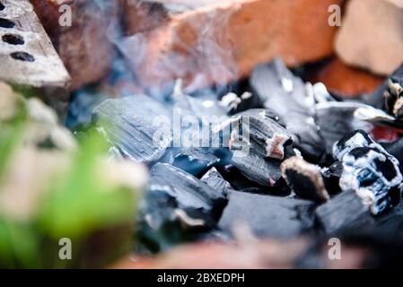 Le braci di un fuoco morto sono fumo nella recinzione di mattoni. Il fuoco dopo il barbecue. Foto Stock