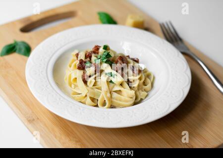 Tradizionale pasta italiana fettuccine Alfredo con pomodori secchi e vegano al basilico. Salsa a base di bechamel, latte vegetale, olio d'oliva Foto Stock