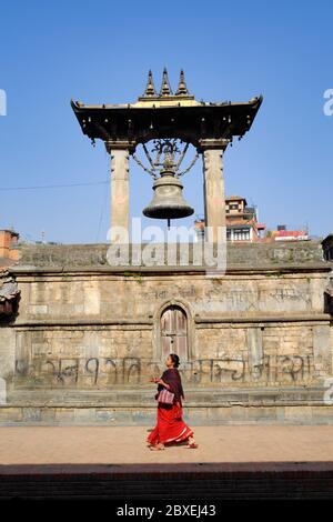 Una donna nepalese, tradizionalmente vestita, passa sotto la Campana Taleju, parte del Tempio Taleju, Piazza Durbar, Patan (Lalitpur), Valle Kathmandu, Nepal Foto Stock