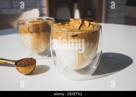 Coffee Dalgona Coffee, un caffè frizzante e cremoso alla moda montato in tazze di vetro su un tavolo bianco con luce naturale Foto Stock