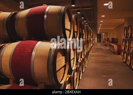 Cantina con lunga fila di botti di rovere impilate per la maturazione del vino rosso. Foto Stock