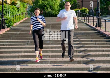 Coppia che corre sulle scale in città, uomo maturo e donna insieme Foto Stock