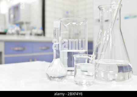 Matraccio, becher e vetreria per laboratorio Chemistry Science con sostanza chimica liquida trasparente su sfondo sfocato. Foto Stock