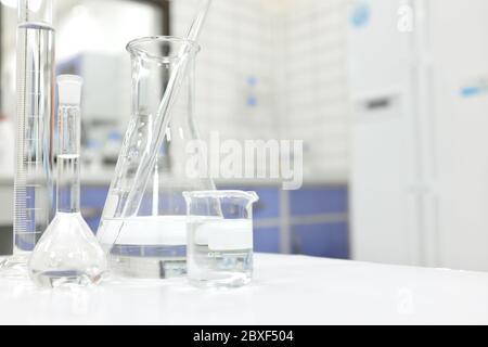 Matraccio, becher e vetreria per laboratorio Chemistry Science con sostanza chimica liquida trasparente su sfondo sfocato. Foto Stock