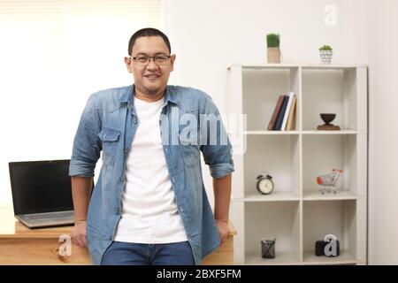 Felice giovane imprenditore asiatico di successo sorridendo alla telecamera con fiducia nel suo studio di casa, il concetto di lavoro a casa Foto Stock