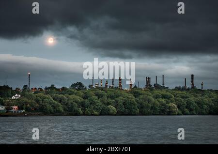 WhiteGate, Cork, Irlanda. 7 giugno 2020. La Luna disperde dietro le torri di distillazione della raffineria di petrolio Irving a Whitegate, Co. Cork, Irlanda. Il tempo è fresco, piuttosto nuvoloso e soprattutto secco oggi. Questo pomeriggio, con gli incantesimi soleggiati in via di sviluppo, si illuminano di più. Moderate brezze da nord a nord-ovest, fresche nelle aree costiere di questa mattina e pomeriggio alti da 16 a 18 gradi Celsius. - credito; David Creedon / Alamy Live News Foto Stock