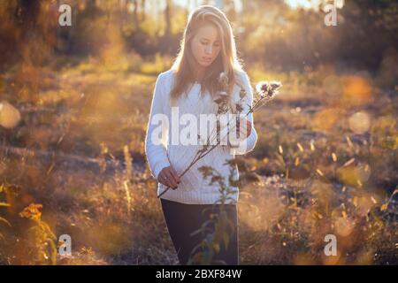 Giovane donna attraente che si posa in un campo con fiori secchi . Verticale con retroilluminazione del sole Foto Stock