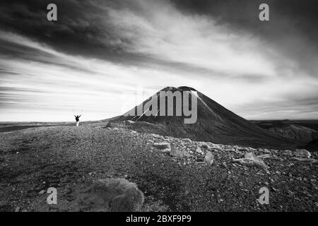 Immagine in bianco e nero di un tramper solista che solleva le braccia con i pali da trekking, salutando il Monte Ngauruhoe sul Tongariro Alpine Crossing, Nuova Zelanda Foto Stock