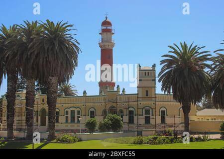 Swakopmund, Namibia - 18 aprile 2015: Antico faro bianco e rosso tedesco, chiamato "bacon", circondato da palme Foto Stock