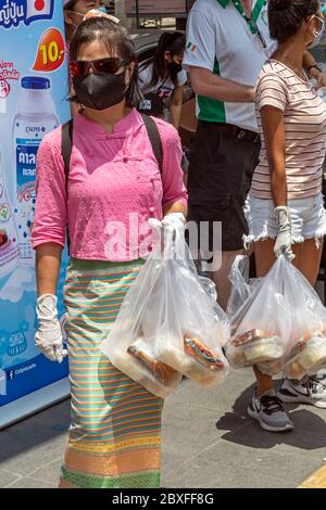 Volontari con maschera facciale e guanti che danno fuori cibo gratuito presso la banca alimentare durante la pandemia di Covid, Bangkok, Thailandia Foto Stock