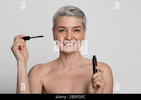 Bella donna matura che tiene aperto mascara in mani e sorridente a macchina fotografica Foto Stock