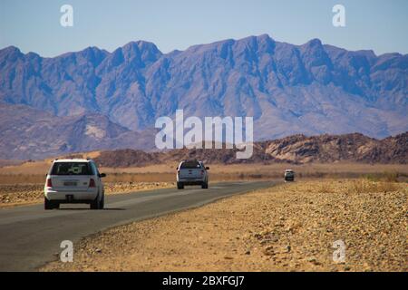 Sossusvlei, Namibia - 28 aprile 2015: Le auto con i turisti viaggiano tra i paesaggi mozzafiato del deserto del Namib, circondato da montagne Foto Stock
