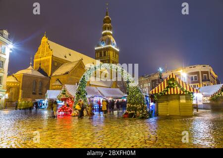 RIGA, LETTONIA - 2 GENNAIO 2017: La Cattedrale di riga Doms e le bancarelle dei mercatini di Natale a Ratslaukums di notte in inverno. Si può vedere la gente. Foto Stock