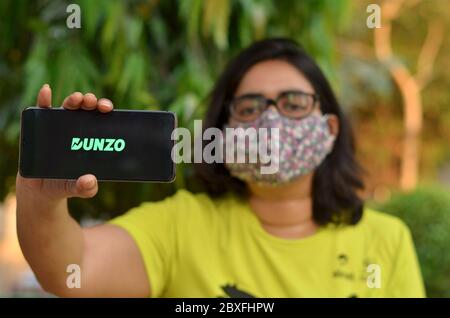 Nuova Delhi, India, 2020. Ragazza che indossa la maschera con il logo dell'app Dunzo Delivery che illumina lo schermo del telefono cellulare nelle sue mani. Messa a fuoco selettiva e de superficiale Foto Stock
