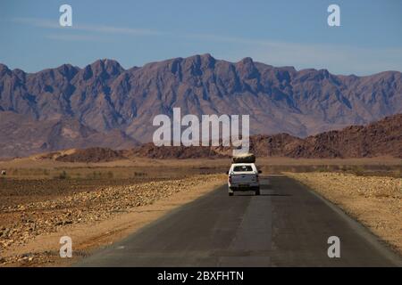 Sossusvlei, Namibia - 28 aprile 2015: Le auto con i turisti viaggiano tra i paesaggi mozzafiato del deserto del Namib, circondato da montagne Foto Stock